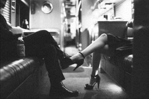Black-and-white shot of a woman's stiletto resting on a man's knee across a train aisle
