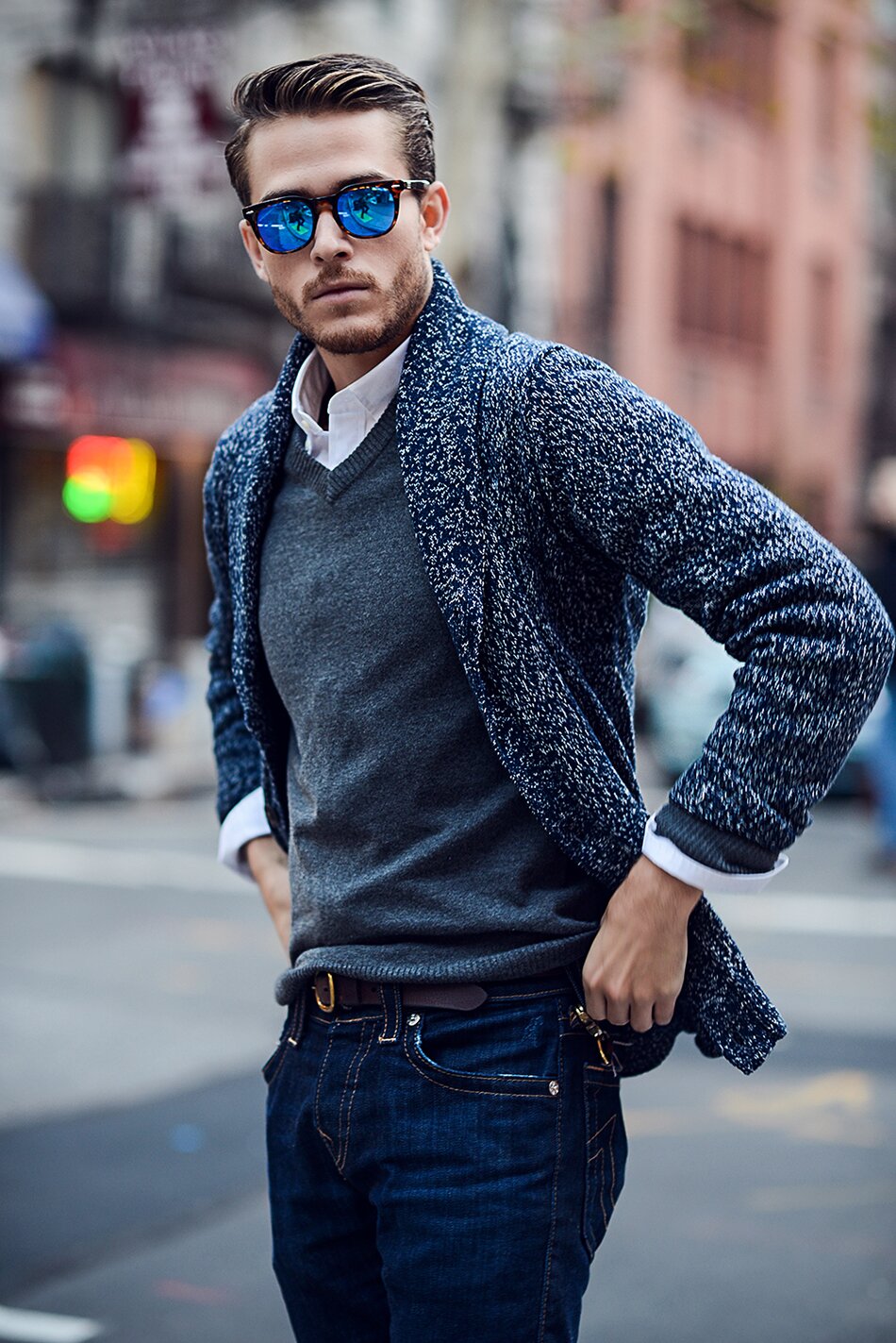 Man in blue mirrored sunglasses, navy marled shawl cardigan, and dark jeans on a city street