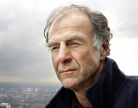 Close-up of an older grey-haired man in a navy fleece, weathered face against a cloudy city skyline