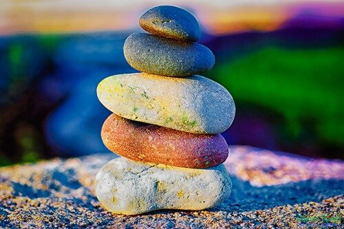 Five smooth multicolored stones stacked in a cairn on sand against a vivid blurred backdrop