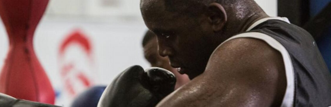 Profile of a sweating Black boxer in black gloves and tank top looking down in a gym