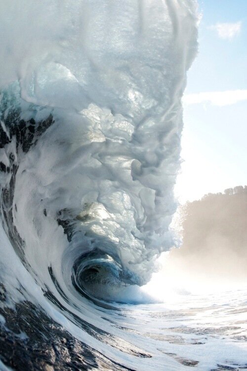 Powerful ocean wave curling into a barrel of thick white foam under bright hazy sunlight
