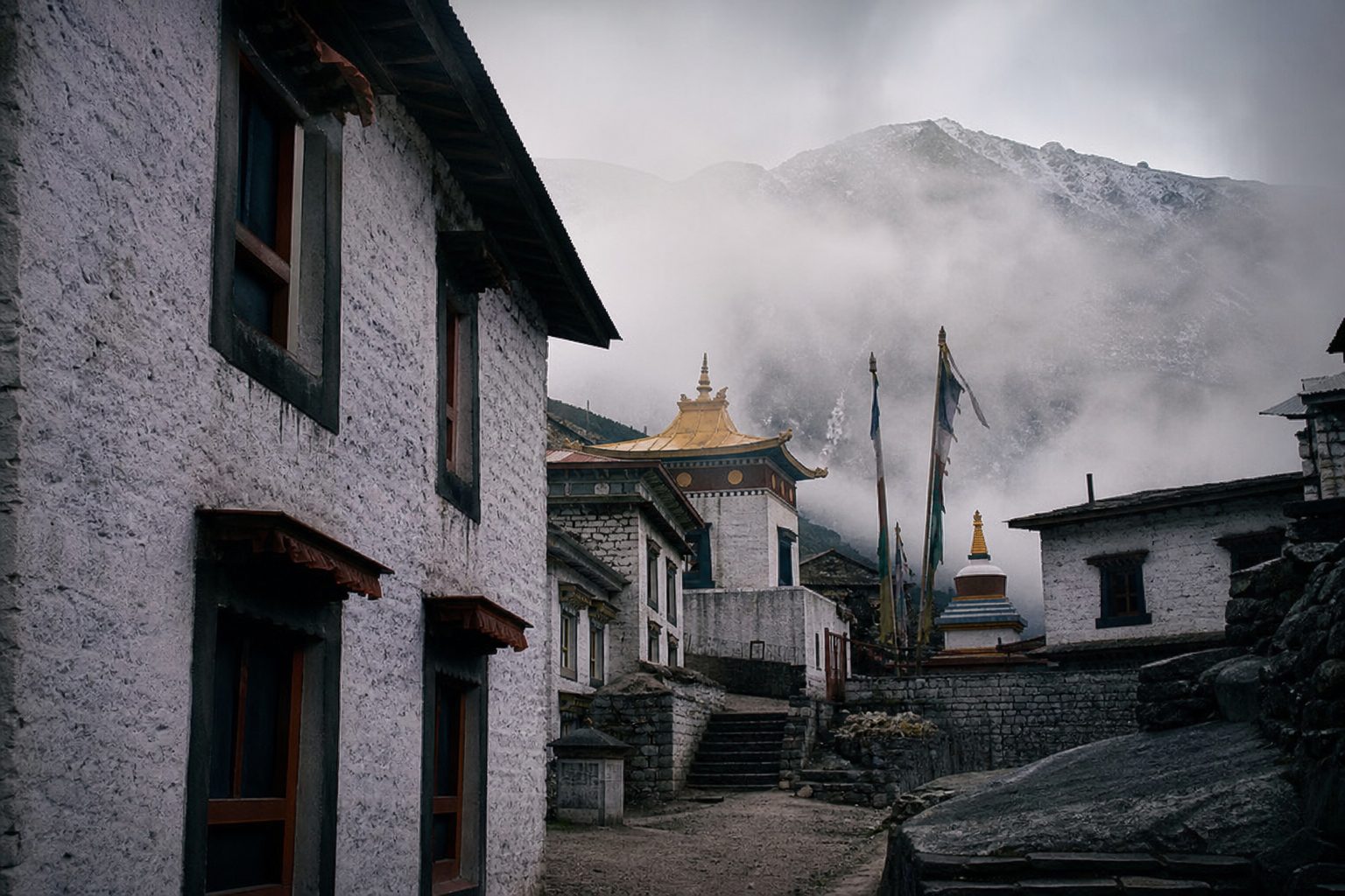 Tibetan Buddhist monastery buildings with prayer flags against misty mountain peaks at dawn