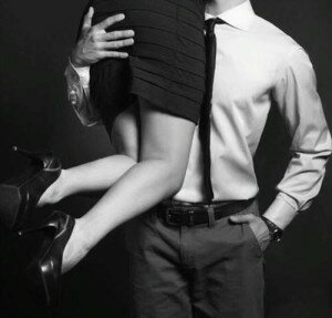Black-and-white studio shot of a man in a dress shirt carrying a woman in a short skirt and heels