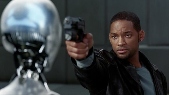 Will Smith in a black jacket aims a handgun at a silver humanoid robot from I, Robot