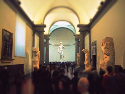 Crowded Accademia gallery looking toward Michelangelo's David with unfinished Prisoners along the hall