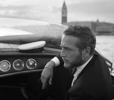 Black-and-white profile of a man in a suit and bow tie seated in a vintage motorboat