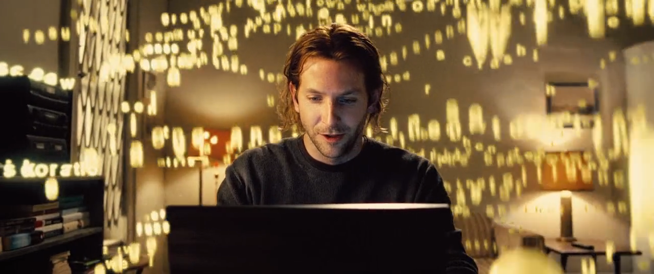 Man intently watching a laptop while glowing golden letters float around him in a dim room
