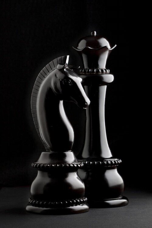 Polished black chess knight and queen pieces lit dramatically against a solid black background