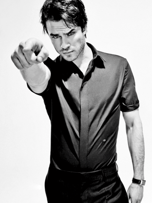 Black-and-white studio shot of a man in a dark short-sleeve shirt pointing his finger at the camera