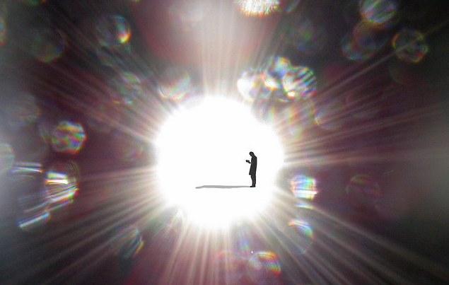 Silhouette of a person inside a blazing white light burst with prismatic rainbow bokeh circles