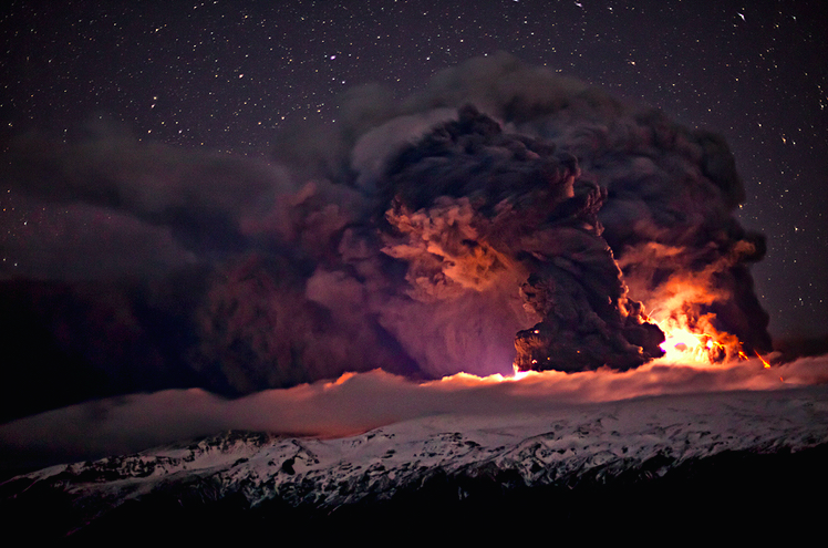 Nighttime volcanic eruption with glowing lava, towering ash cloud, snowy peaks, and starry sky