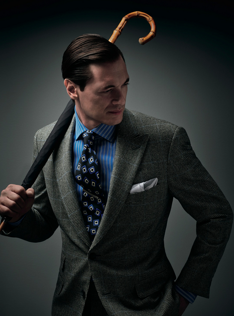 Man in a grey check blazer and blue striped shirt holding a bamboo-handled umbrella over his shoulder