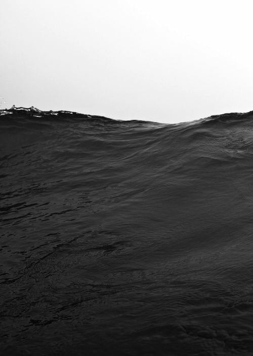 Large dark ocean swell rising against a stark white sky in high-contrast black and white