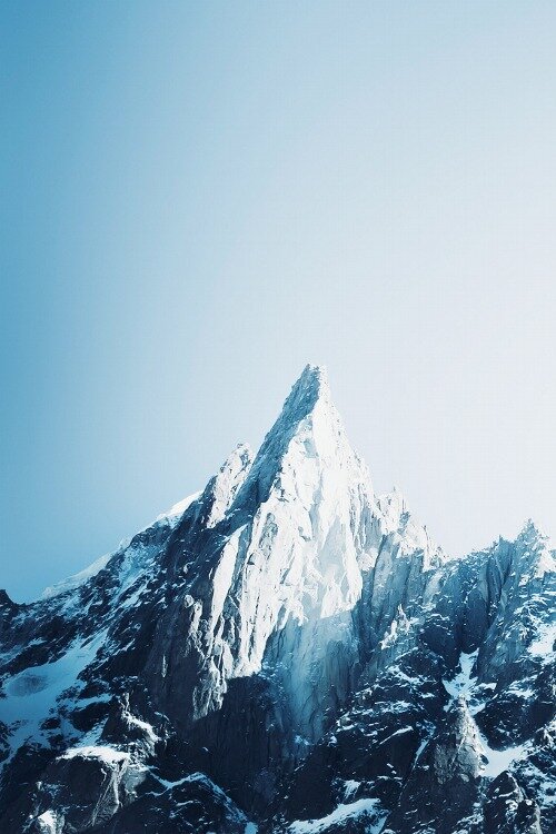 Sharp snow-capped mountain peak with jagged rocky faces against a clear blue sky