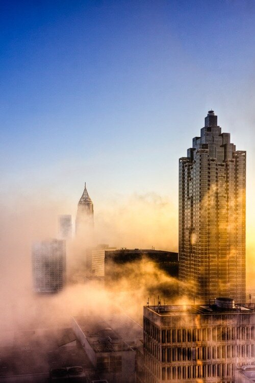 Atlanta skyscrapers emerging from thick golden fog under a clear blue sky at sunrise