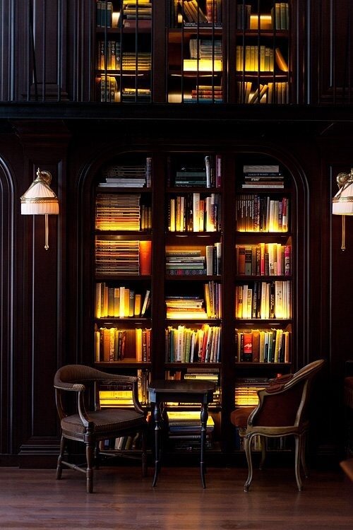 Dark wood library alcove with warm backlit bookshelves and two vintage reading armchairs
