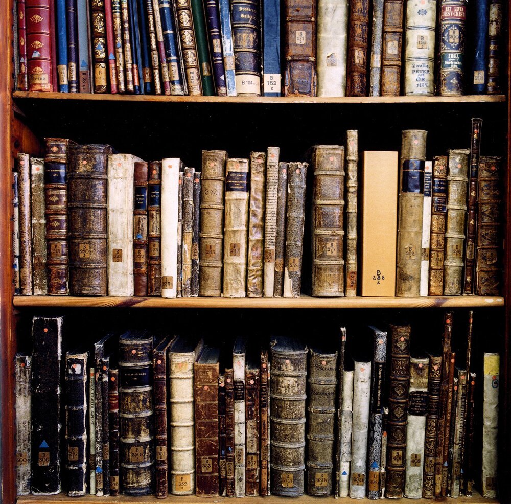 Three shelf rows packed with antique leather-bound books showing worn spines and library labels