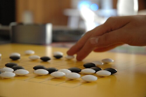 Close-up of a Go board as a hand places a white stone among black and white stones