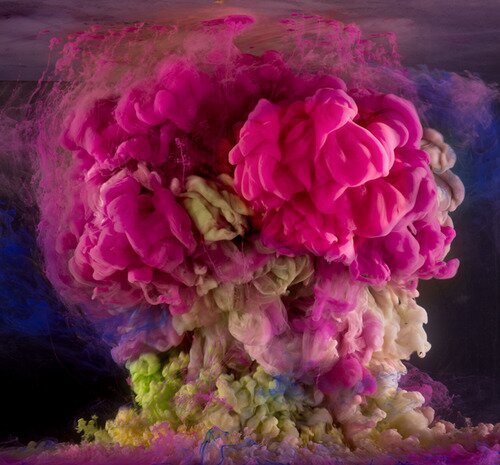 Macro plume of magenta, pink, white, and green ink swirling like a bloom in dark water