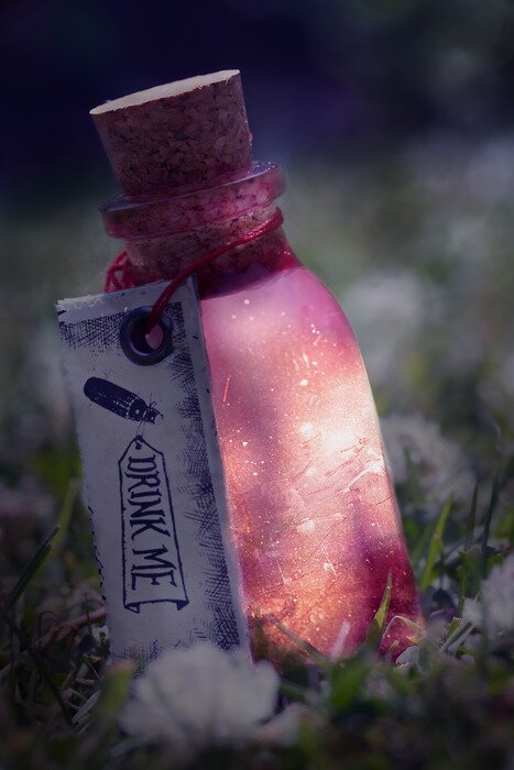 Glowing pink potion bottle with a Drink Me tag nestled in grass and small white flowers