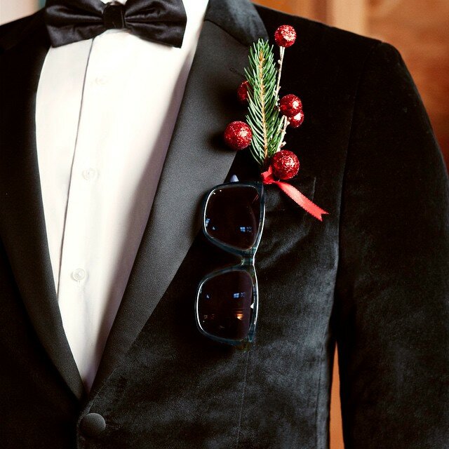 Black velvet tuxedo with pine sprig and glittery red berries boutonniere, sunglasses in the pocket