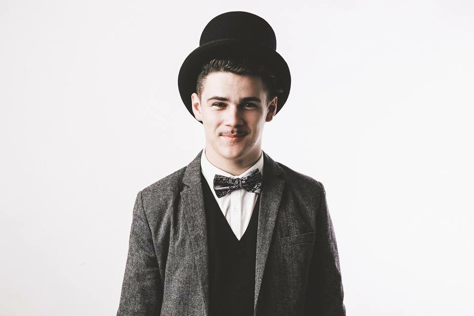 Smiling young man in a black bowler hat, tweed blazer, waistcoat, and patterned bow tie