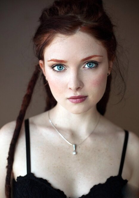 Young woman with bright blue eyes and auburn dreadlocks in a black lace top and silver pendant