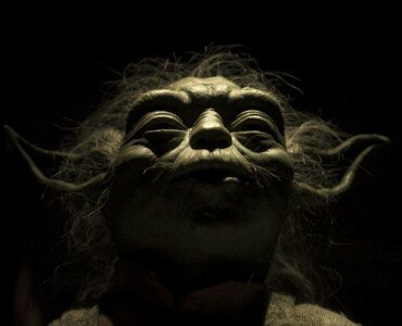 Dramatic low-angle close-up of Yoda with eyes closed, lit from above against a black background